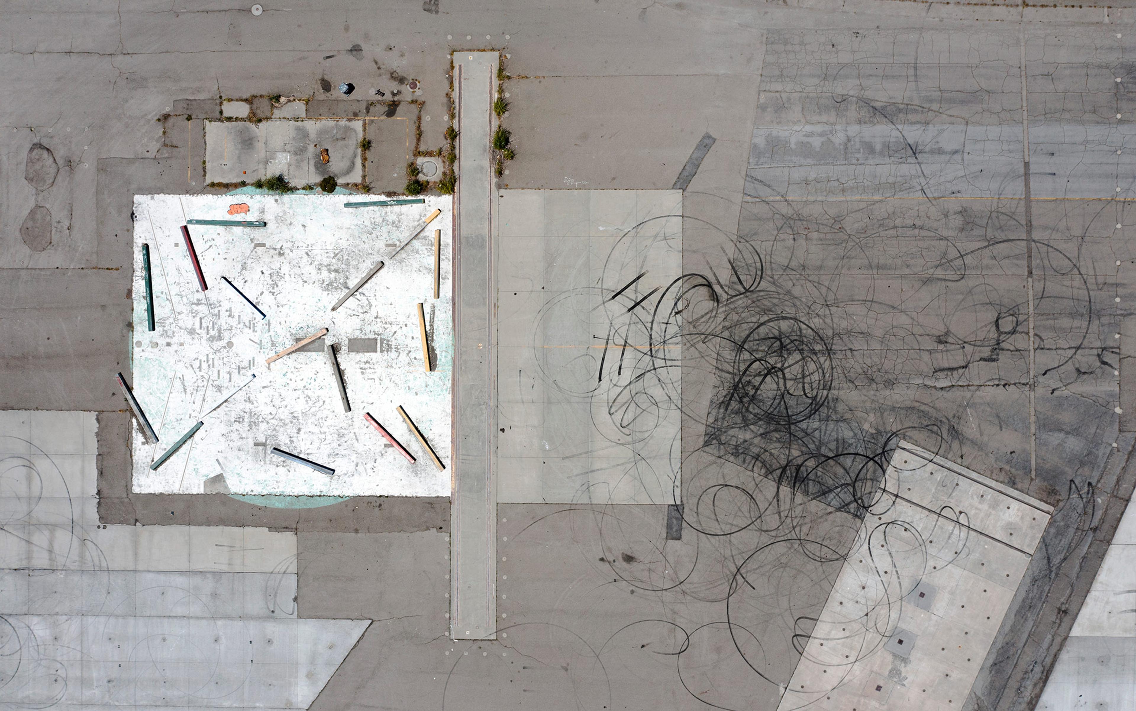 Aerial view of a concrete area with colourful staggered beams, sections of white paint, and black tyre marks forming circular patterns.