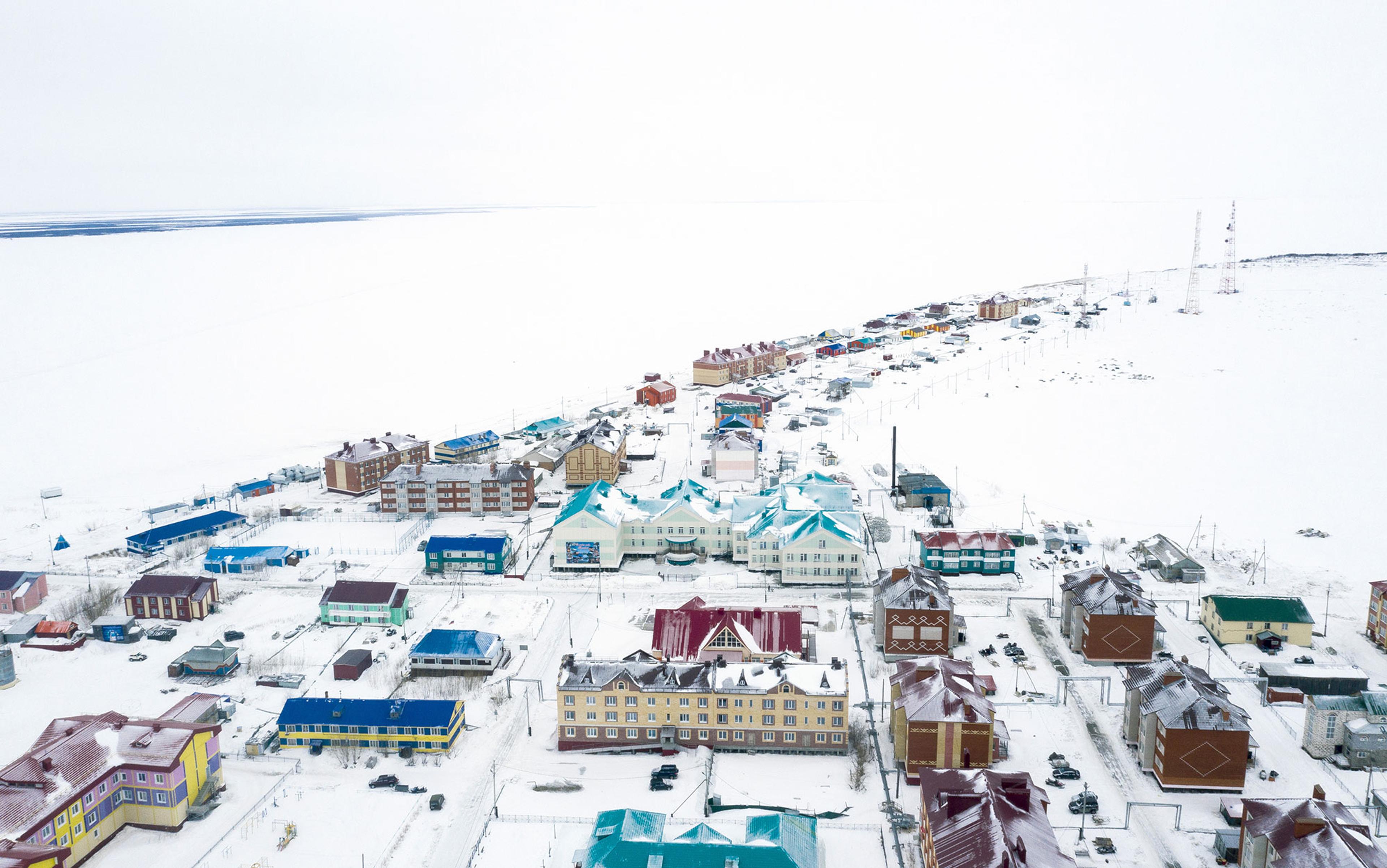 Aerial photo of a snowy town with colourful buildings and a vast frozen landscape in the background.